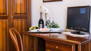 A wooden desk with a bottle of wine, a glass, a bowl of fruit, and a plate of food.