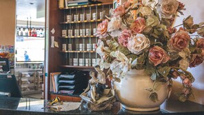 A vase with flowers on a counter, a small statue, and a shelf with books and items in the background.