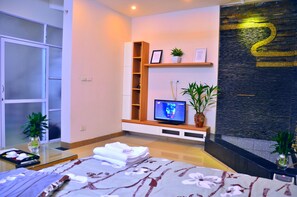 A modern hotel room with a bed, a television, a small shelf with plants, and a decorative wall number. - Mia House Hanoi Central (Hanoi)