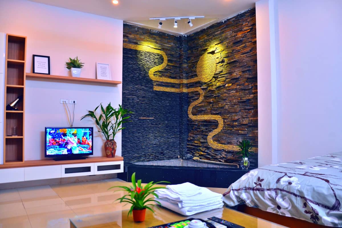 Habitació d'hotel moderna amb televisió, una paret decorativa, un llit i una taula petita amb una planta.