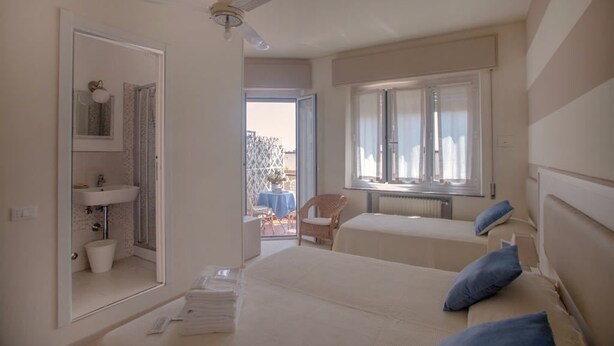 A bedroom with two beds, a window, a ceiling fan, and a bathroom visible through an open door. - Locanda Kon Tiki (Alassio)