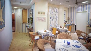 A dining area with striped walls, wicker chairs, and tables with blue and white tablecloths. - Locanda Kon Tiki (Alassio)