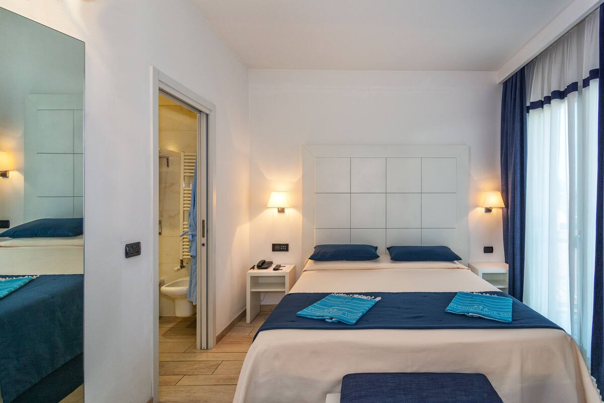 A hotel room with two beds, a bathroom, and a view of the outside.
