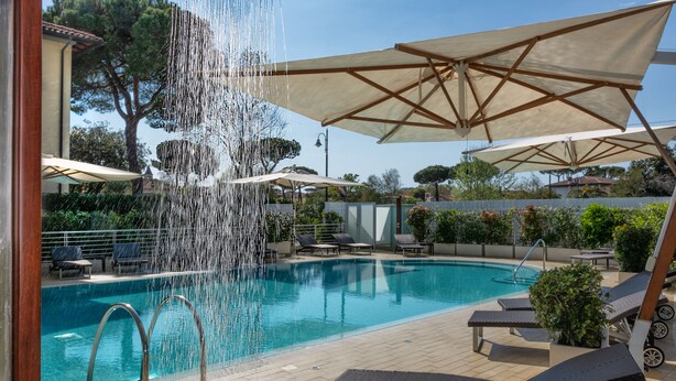 A swimming pool with a water feature, sun loungers, and umbrellas. - Hotel Central Park (Pietrasanta)