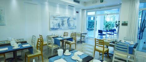 A dining area with multiple tables set for service, chairs, and a large window providing a view of the outdoors.