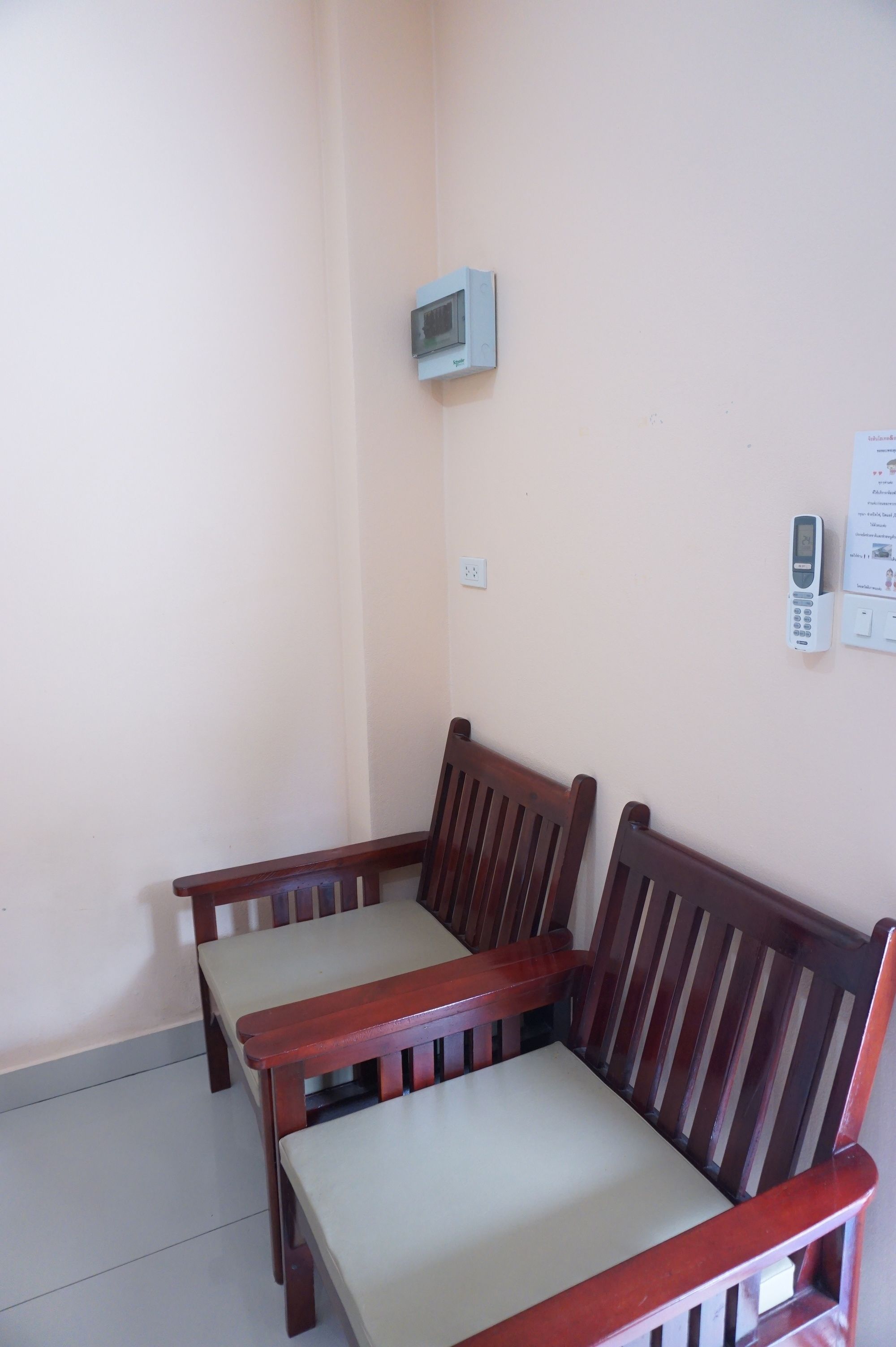 Une petite pièce avec deux chaises en bois et une table, un climatiseur fixé au mur et un téléphone fixé au mur.