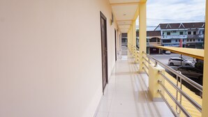 Un couloir avec une rambarde jaune, des portes et une vue sur des immeubles et des voitures garées.