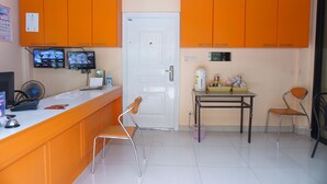 Une cuisine avec des meubles de couleur orange, une porte blanche, une petite table avec des chaises et deux écrans fixés au mur.
