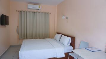 A neatly made bed with white linens, a bedside table with a folder, a wall-mounted TV, and an air conditioning unit.