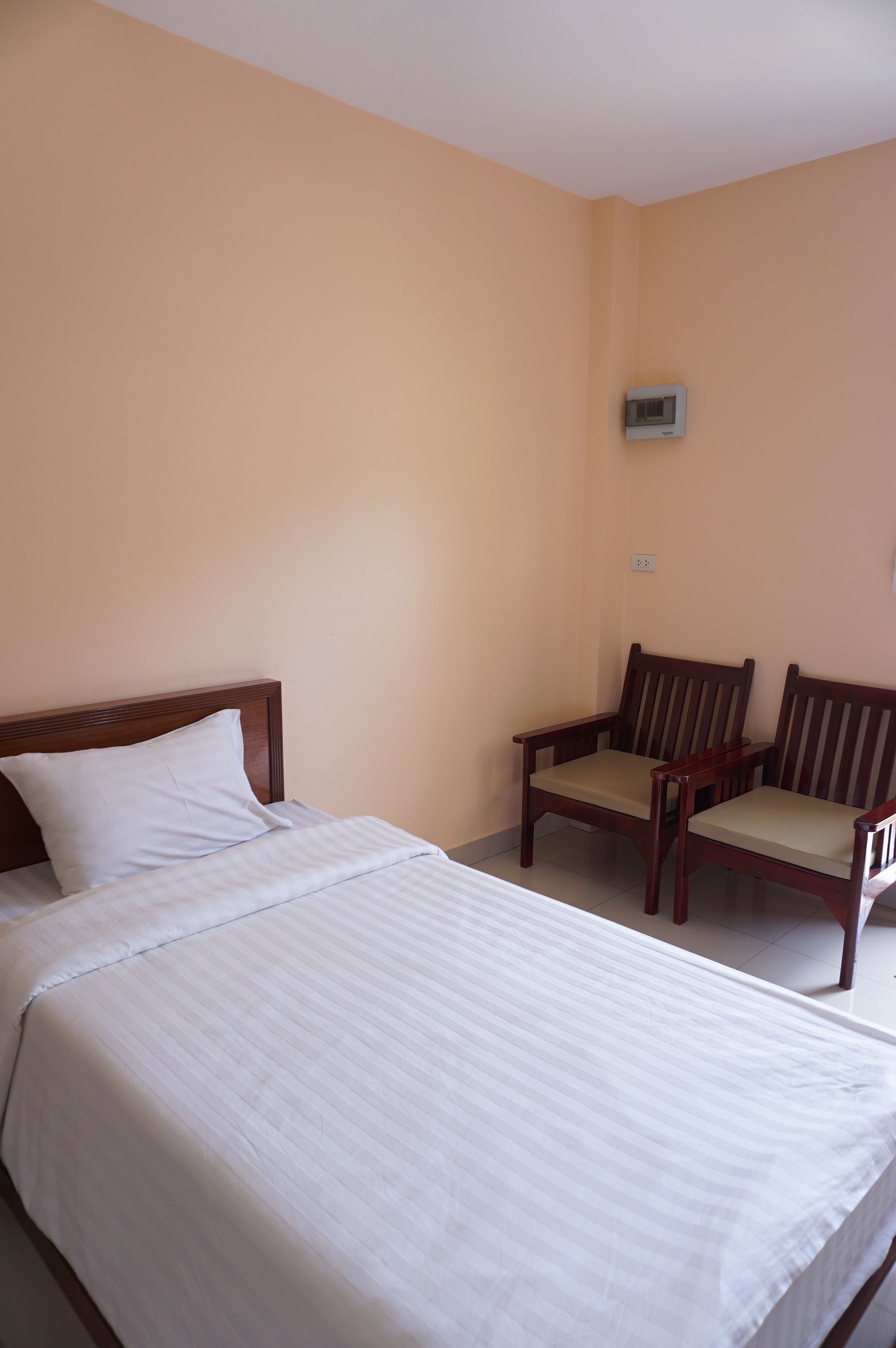 A bedroom with a bed, two wooden chairs, and a thermostat on the wall.