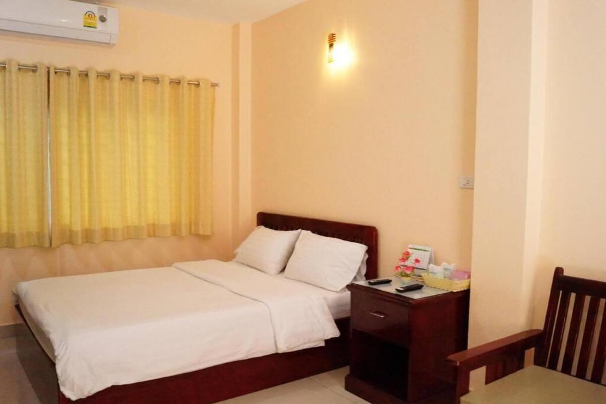 Una habitación de hotel con cama, mesita de noche, silla y ventana con cortinas.