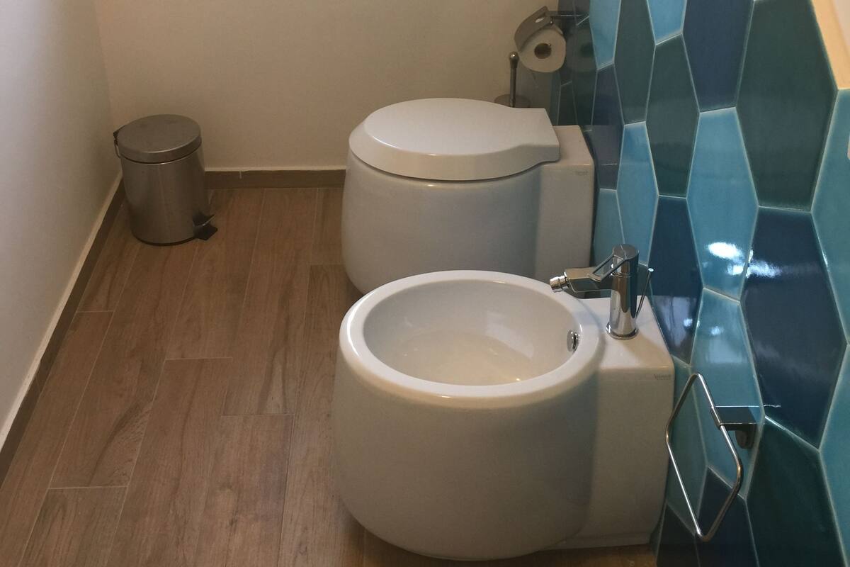 A bathroom with a toilet, bidet, and a trash can.