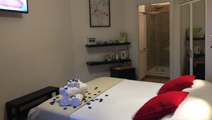 Habitació d'hotel amb un llit, una zona de dutxa i una televisió penjada a la paret.