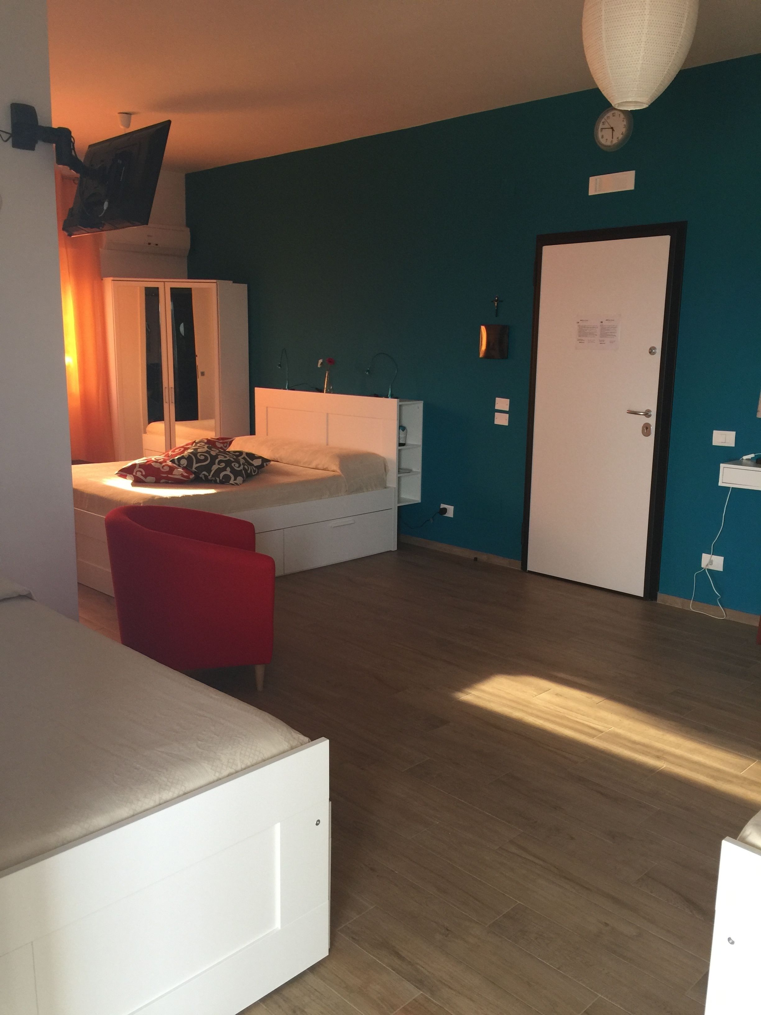 A bedroom with a bed, a wardrobe, a red chair, a desk, and a white wardrobe.