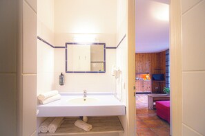 A bathroom with a white sink, mirror, and towel rack. There is a wooden floor and a pink chair in the adjacent room. - Garden & City Bagnères-de-Bigorre - Domaine de Ramonjuan (Bagnères-de-Bigorre)