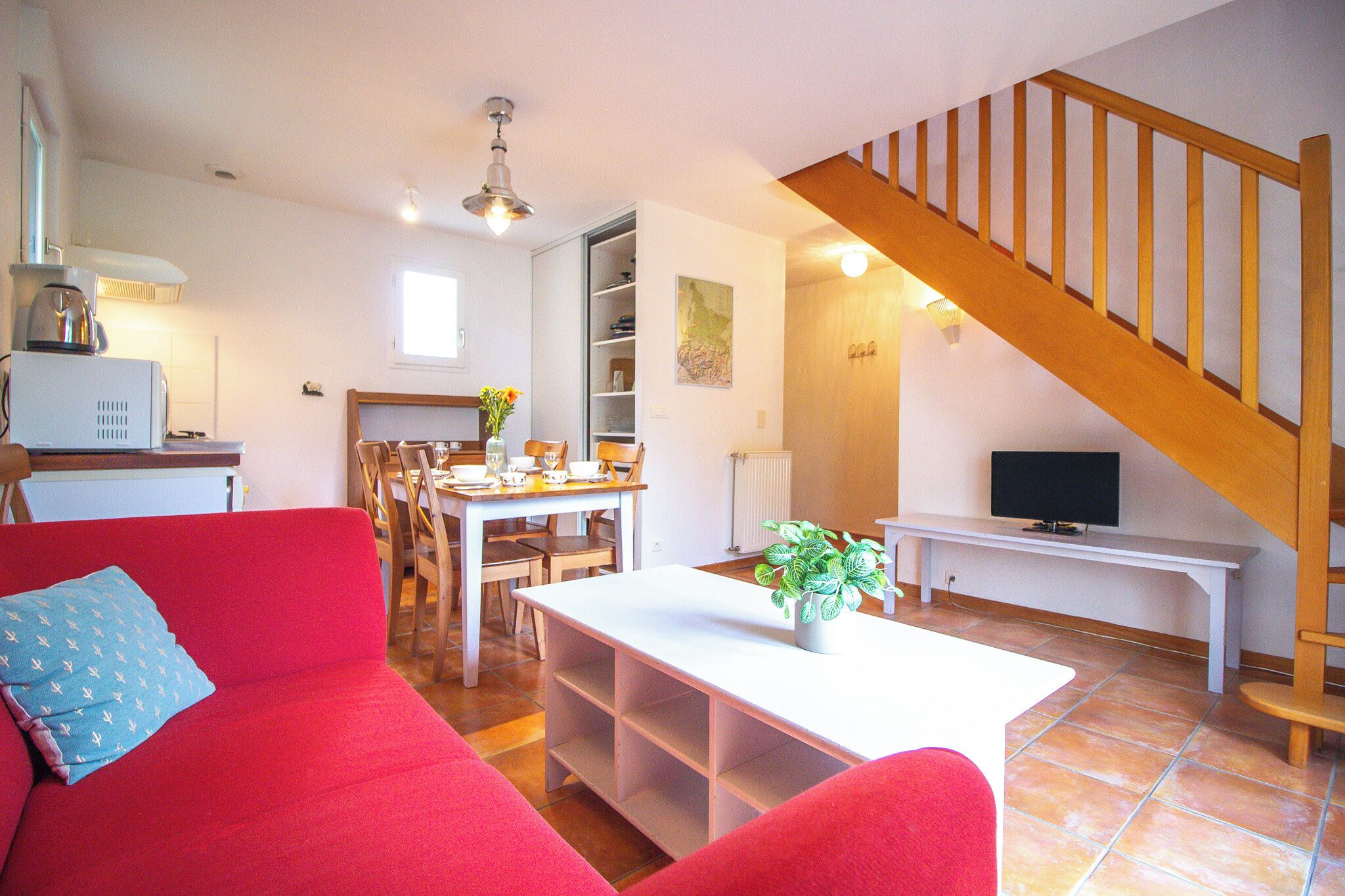 A living room with a red sofa, a white coffee table, a TV, and a wooden staircase.
