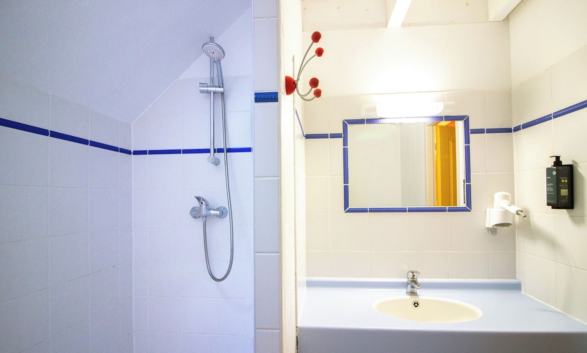 A bathroom with a shower, sink, mirror, and toiletries.