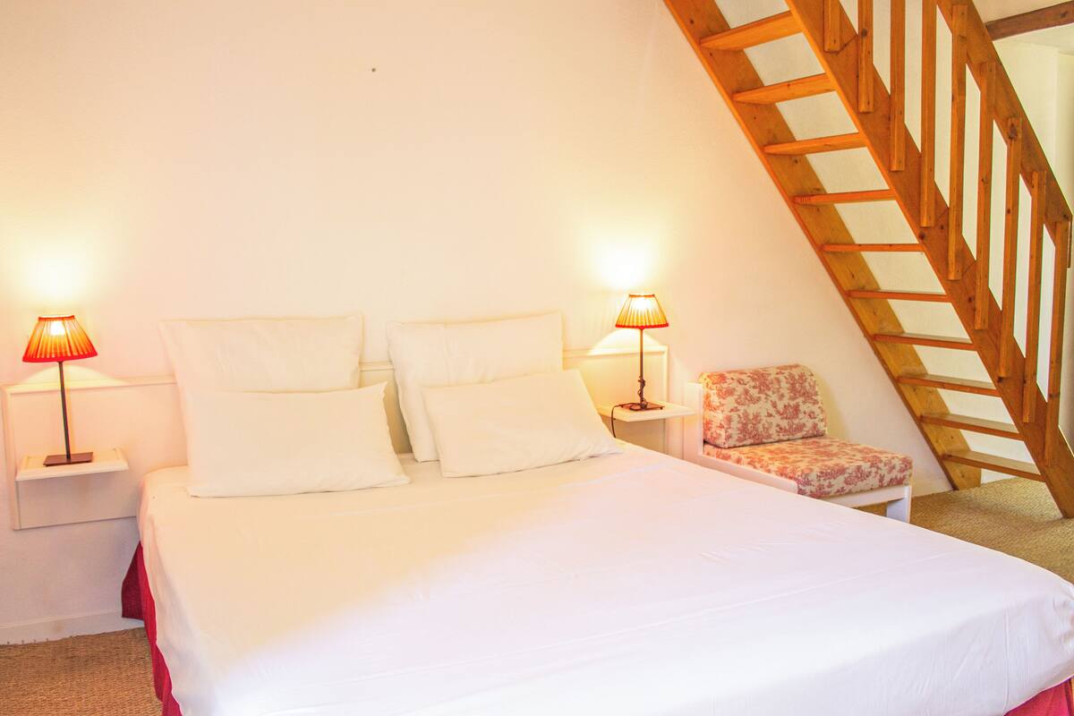 Une chambre à coucher avec un grand lit, deux tables de chevet avec des lampes, une chaise et un escalier en bois.