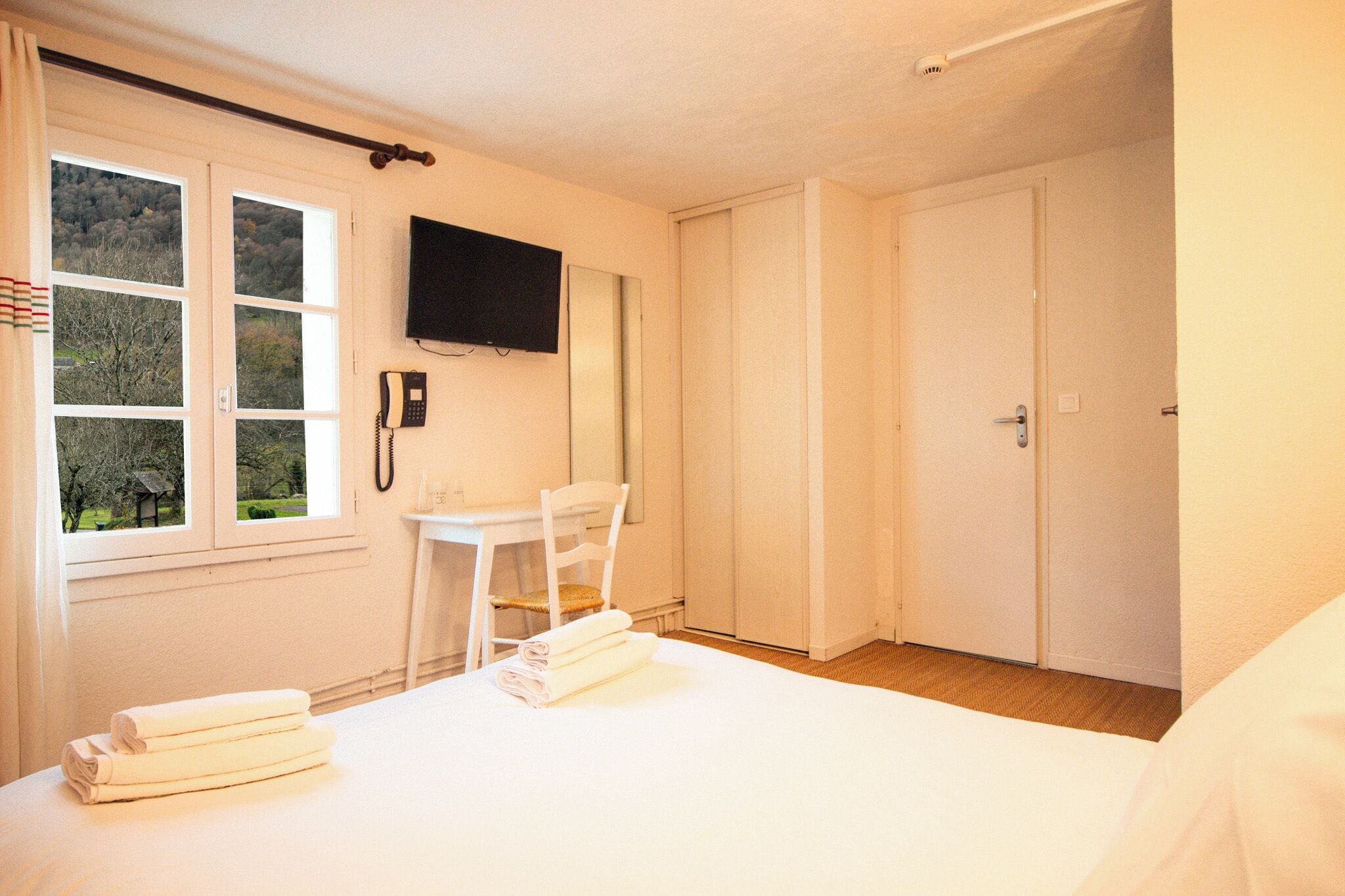 A hotel room with a bed, a desk, a chair, a TV, and a window with curtains.