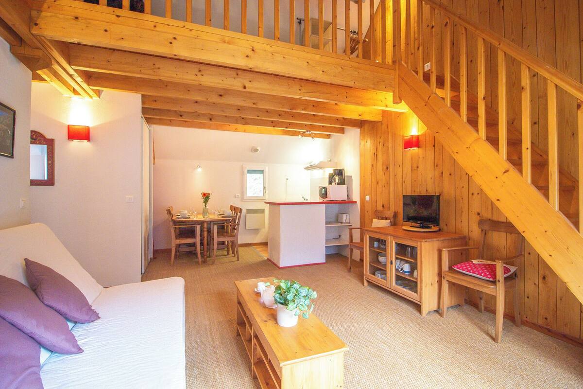 Un intérieur chaleureux avec des éléments en bois, comprenant un canapé, une table en bois agrémentée d’une plante, un téléviseur et un escalier.