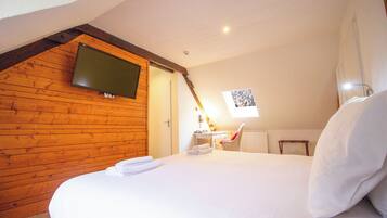 A bedroom with a wooden ceiling, a bed with white linens, a desk with a chair, and a TV mounted on the wall.