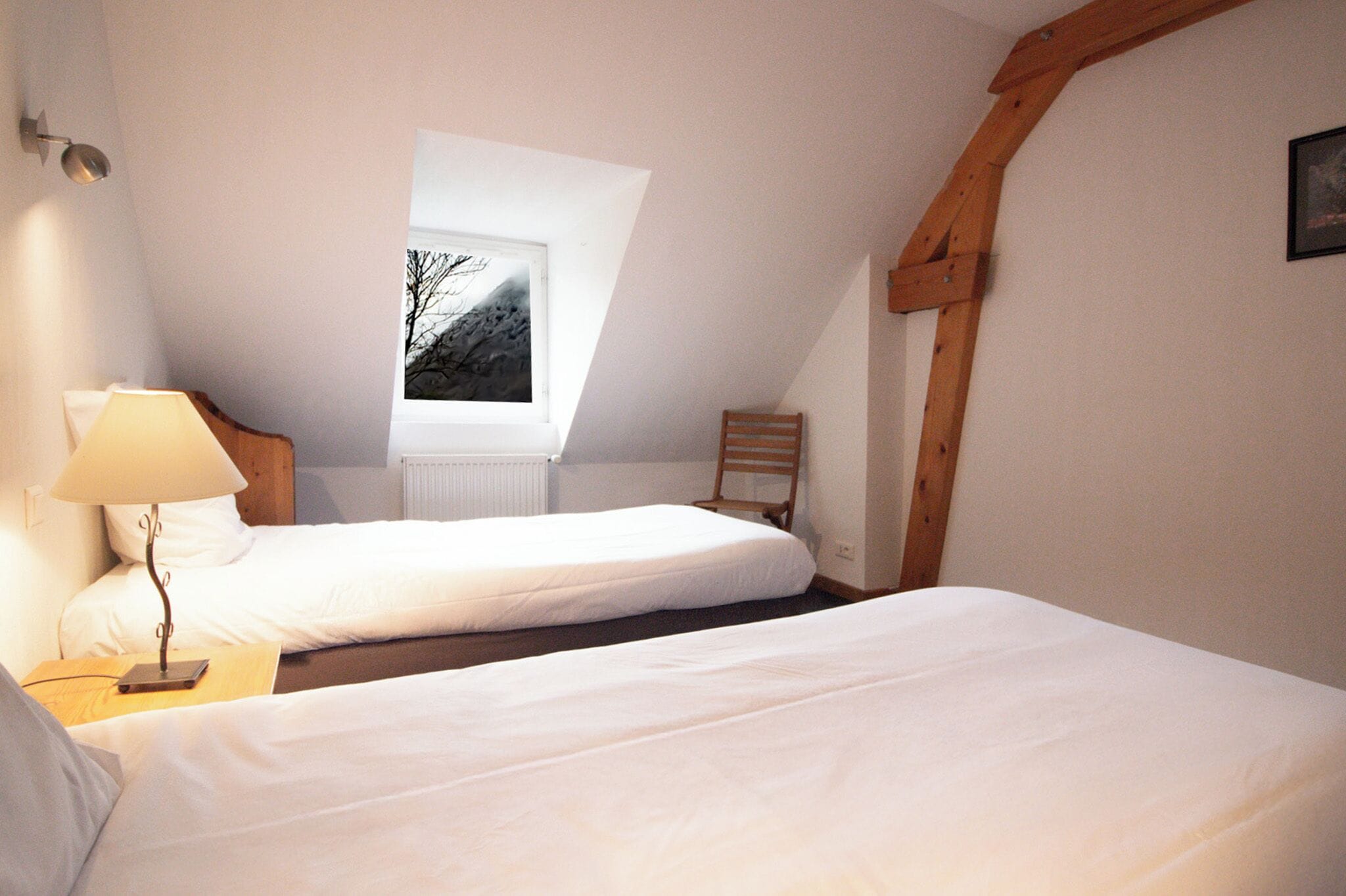 A bedroom with two beds, a window with a view of a mountain, and a wooden ceiling beam.