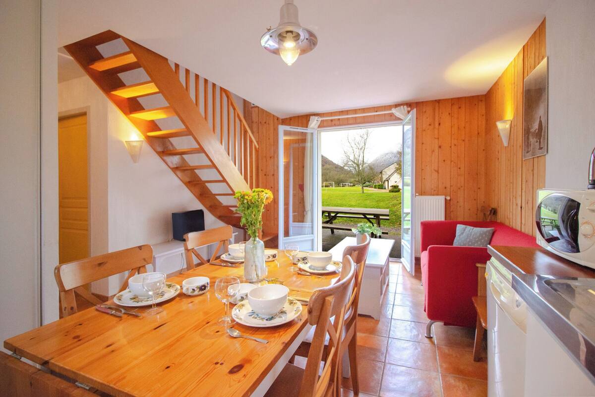 Un coin repas avec une table en bois dressée pour quatre personnes, un canapé rouge et un escalier menant à une autre pièce.