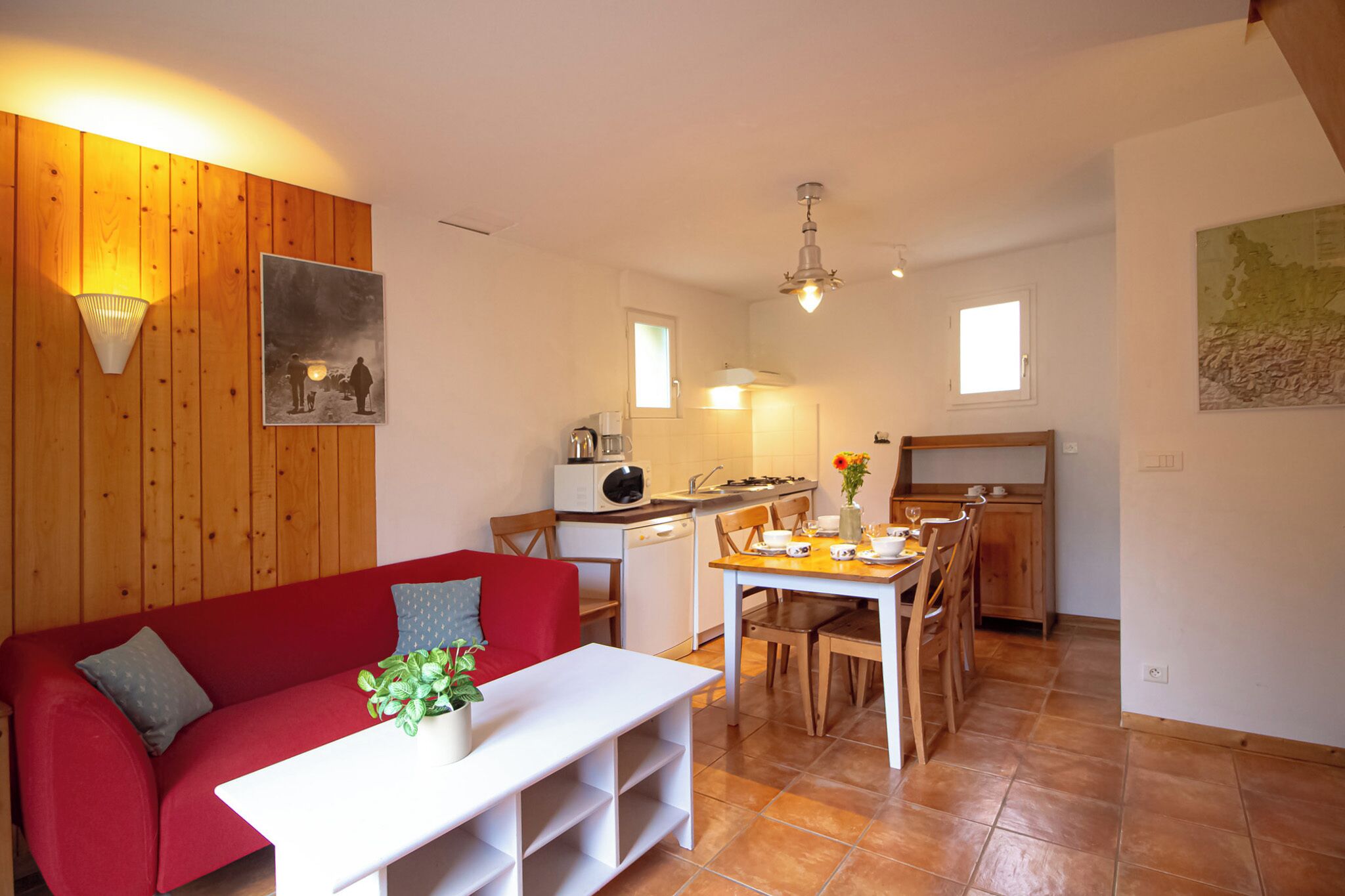 Un espacio habitable compacto con un sofá rojo, una mesa blanca, una zona de cocina con microondas y una mesa de comedor con sillas.