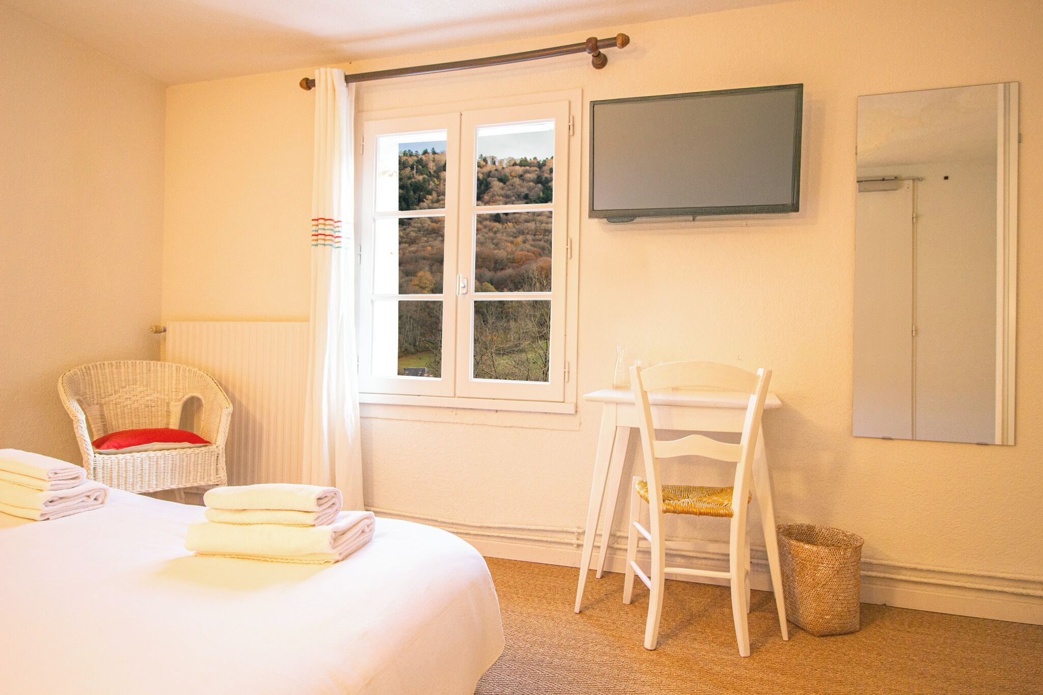Habitación de hotel con cama, una silla, televisor y ventana con vista a árboles.