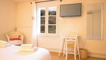 Habitación de hotel con cama, una silla, televisor y ventana con vista a árboles.