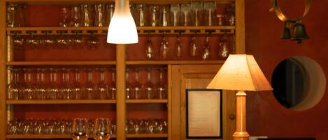 A bar area with a wooden counter, two wine glasses, a hanging light fixture, and a wall-mounted lamp.