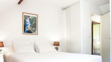 A bedroom with a bed, white walls, a framed picture of a waterfall, and a door leading to another room.