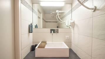 Un baño con lavamanos blanco, espejo y zona de ducha.