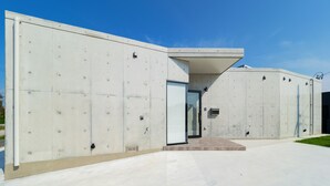 Ein modernes Gebäude mit einer Betonfassade, einem Glastür-Eingang und einem kleinen Außenbereich mit einer Bank.