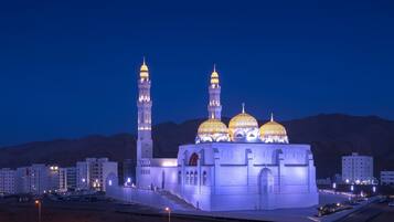 Uma mesquita com três cúpulas e dois minaretes, rodeada por edifícios modernos.