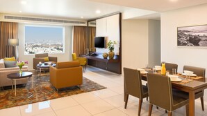 A modern hotel room with a dining area, living space, and a large window with a city view. - Fraser Suites Muscat (Muscat)