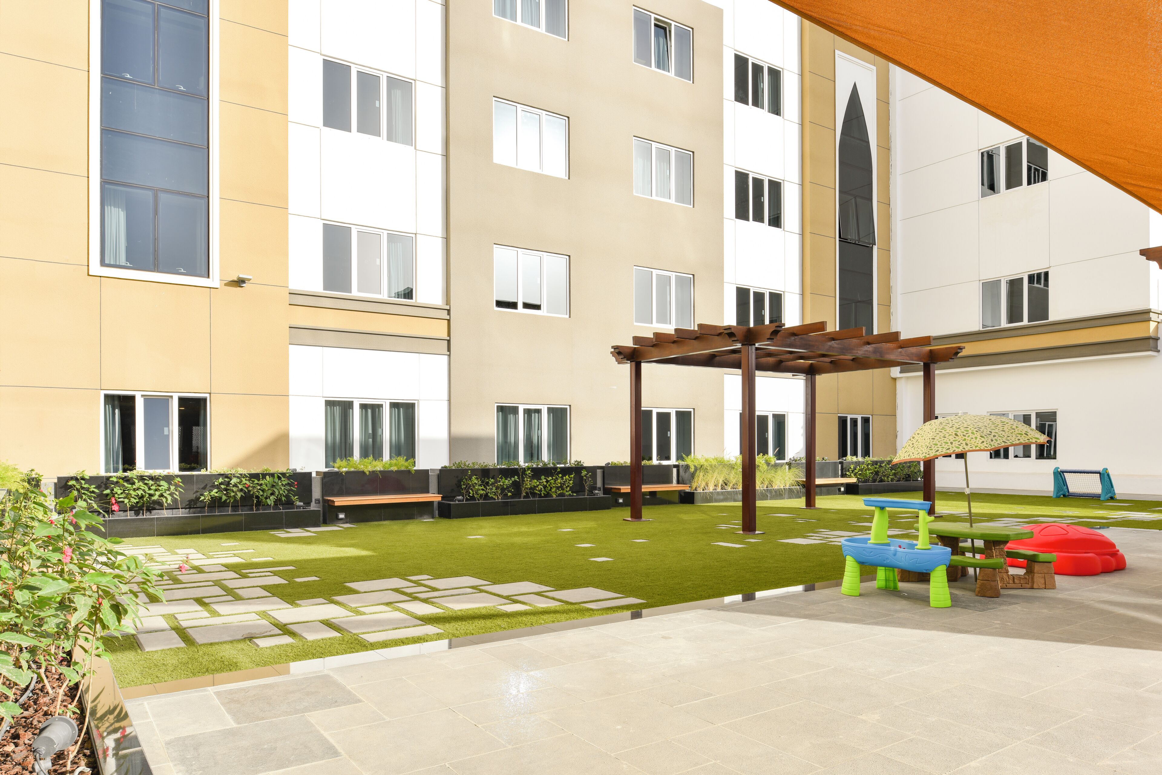 Un patio con una pérgola, una zona de juegos infantiles y un banco.
