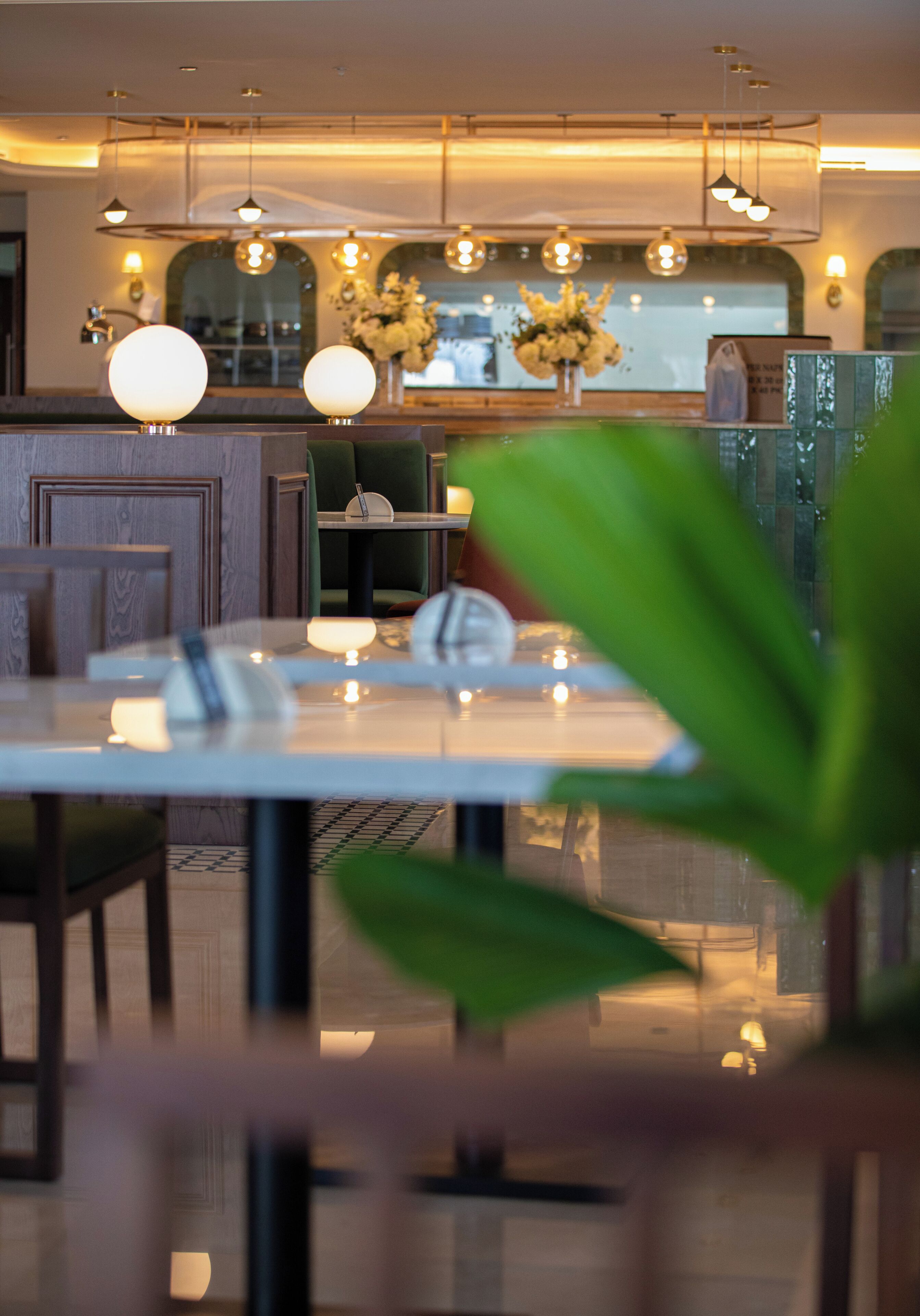 A restaurant interior with a dining table, chairs, hanging pendant lights, and a vase with flowers.