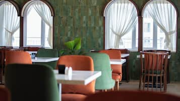 Ein Restaurantinneres mit grünen Fliesenwänden, bogenförmigen Fenstern mit weißen Vorhängen und modernen Möbeln.