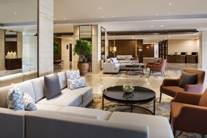 A modern hotel lobby with a seating area, a reception desk, and a dining space.