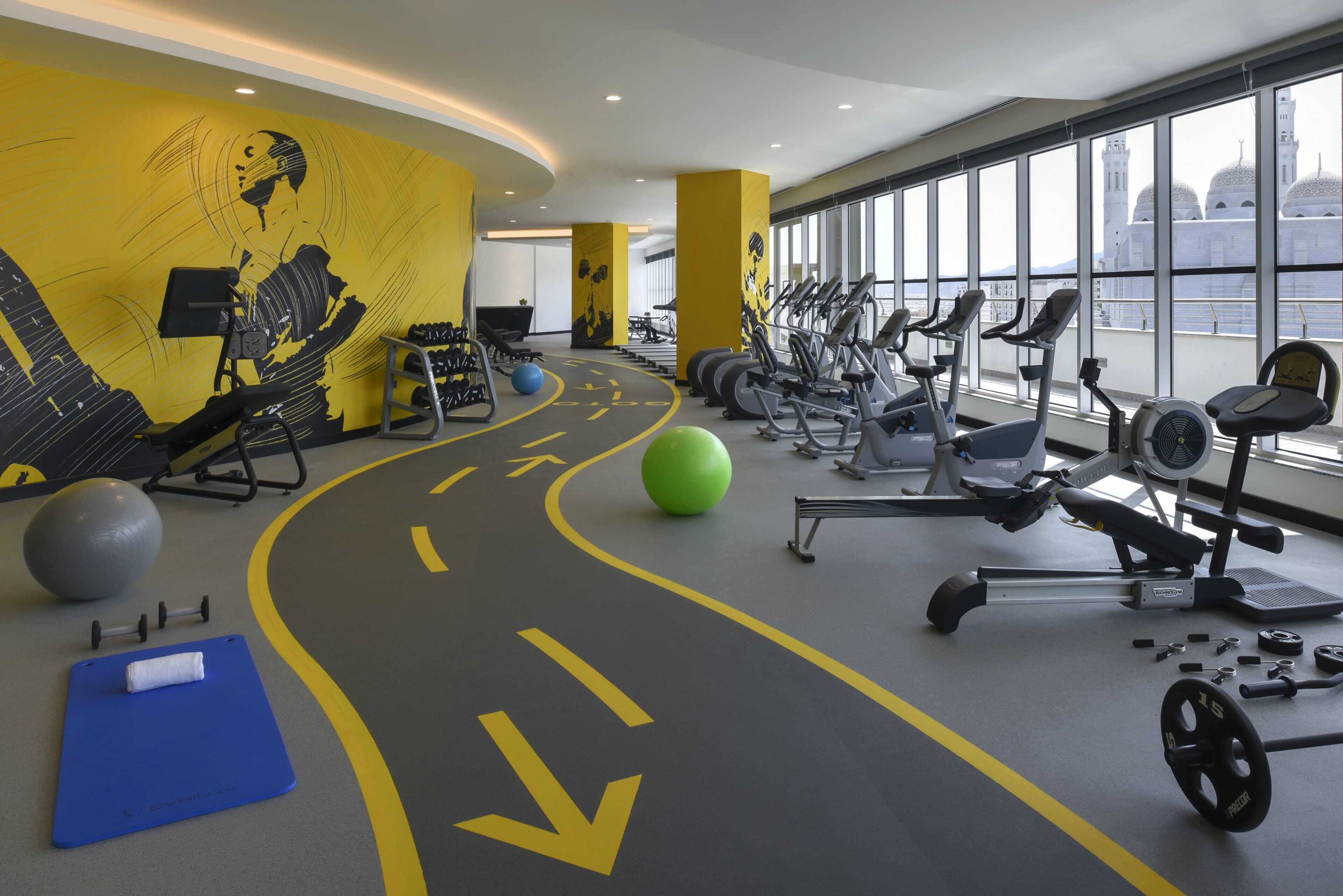 A gym with exercise equipment, a blue mat, and a yellow directional path on the floor.