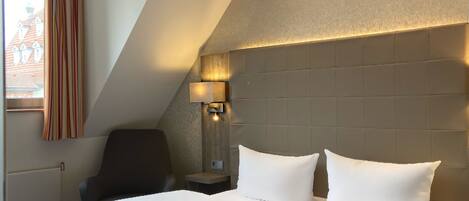 A hotel room with a large bed, a chair, a nightstand, and a lamp.