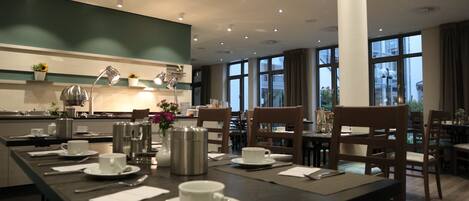 A dining area with a long table set for a meal, chairs, and a view of the city through large windows.