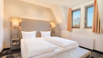 A modern hotel room with a large bed, two bedside tables, a headboard, and a window with curtains.