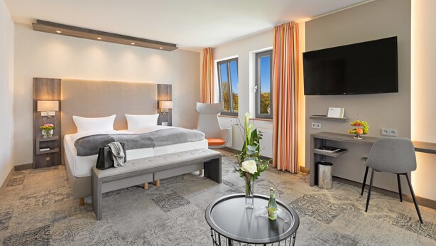 Ett modernt hotellrum med en stor säng, sängbord, ett skrivbord, en platt-TV och utsikt över omgivningarna.
