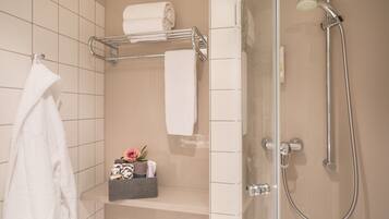 A modern bathroom with a glass-enclosed shower, a towel rack with multiple towels, and a shelf with toiletries and a rose.