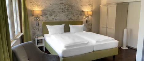 Una habitación de hotel con una cama grande, una silla, un escritorio con un teléfono y un armario.