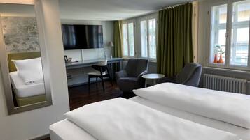 Een hotelkamer met twee bedden, een bureau, een stoel, een televisie en een raam met gordijnen.