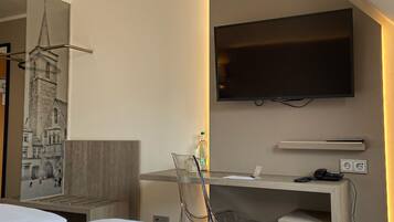 A hotel room with a bed, a desk with a chair, a television, and a trash can.