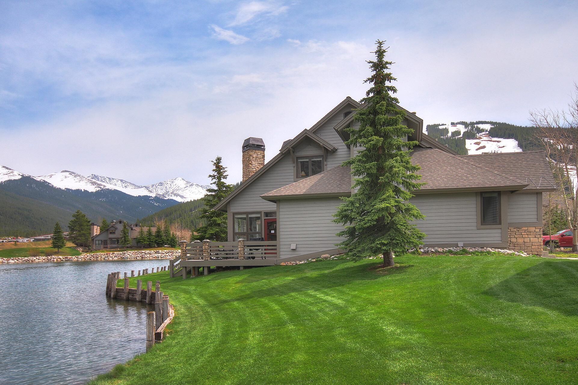 A house with a stone chimney, a deck, and a view of mountains and a lake.